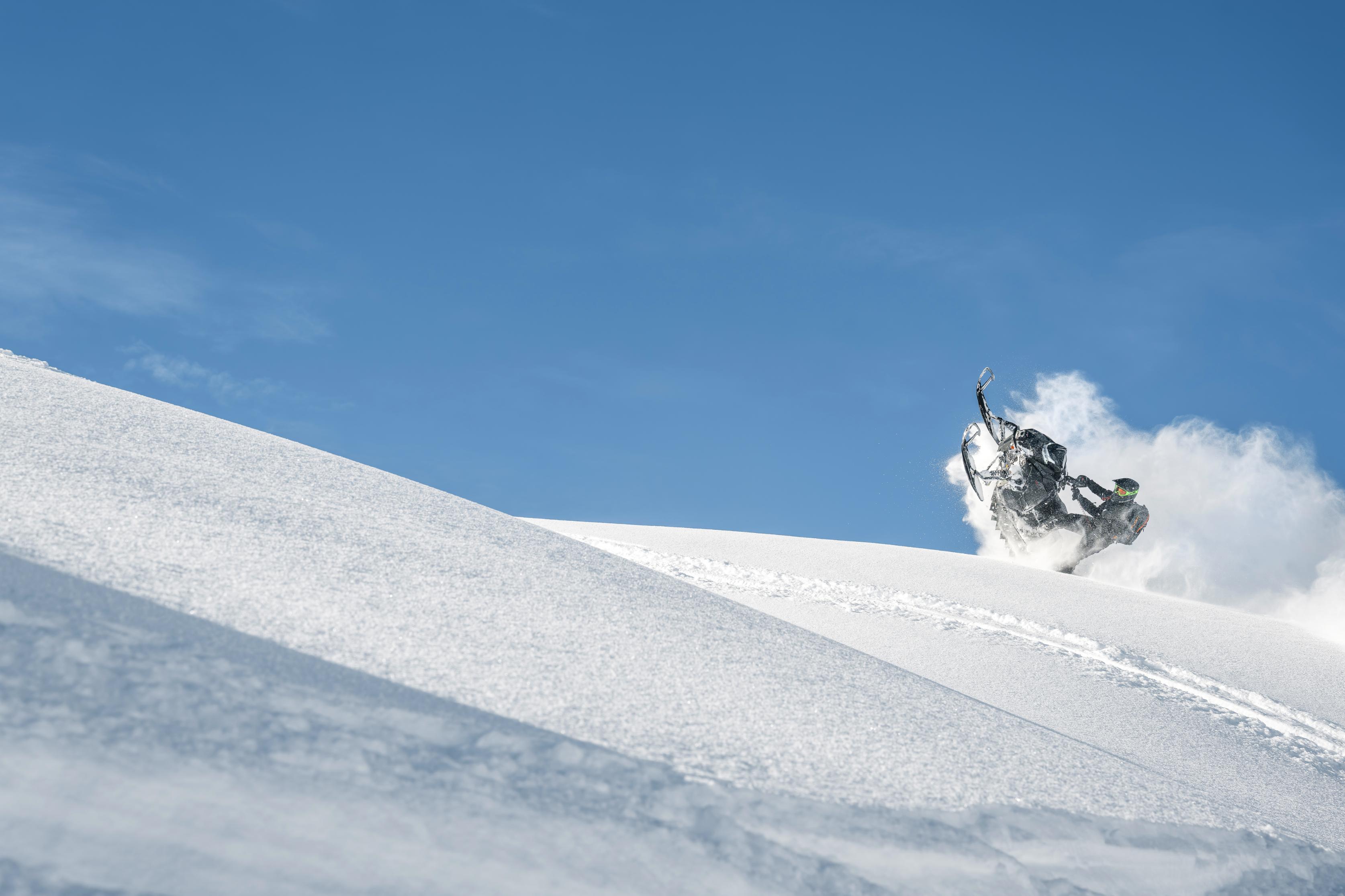 Snøscooter i bratt, snødekt fjellterreng under blå himmel